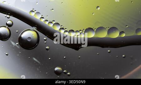 Symmetrical liquid droplets lined along a dark curve with bright yellow backlighting Stock Photo