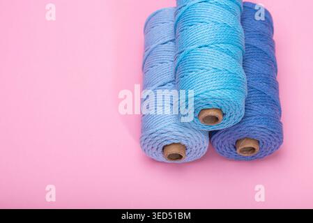 Three spools of woven cord in different shades of blue, displayed on a bright pink backdrop. Stock Photo
