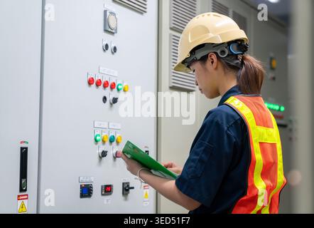 Industrial technician or inspector conducting a safety audit and checking electrical status indicators on a technical control board inside a factory. Stock Photo