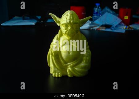 Lime green 3D-printed Yoda Buddha figurine on dark table with workshop background. Stock Photo