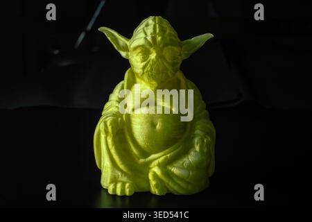 Lime green 3D-printed Yoda Buddha figurine on dark studio background. Stock Photo