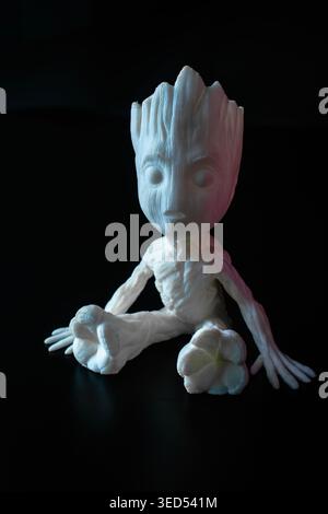 White 3D-printed Baby Groot figurine with pink and blue studio lighting on black background. Stock Photo