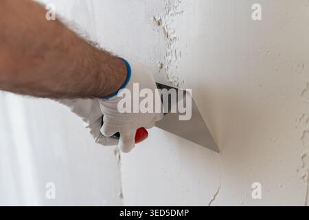 Technician applying finishing plaster using stainless steel trowel on wall surface. Clean working area with smooth drywall texture visible in background. Stock Photo