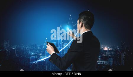 Businessman stands against a city skyline at night, analyzing growth trends using a tablet and digital chart, symbolizing modern financial strategies Stock Photo