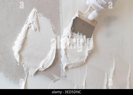 Applying white plaster using a stainless steel spatula on a smooth wall surface. The workspace features a clean and organized environment with subtle gray tones. Stock Photo