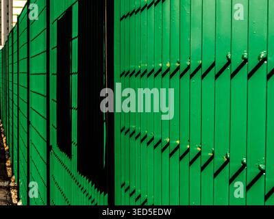 Abstract perspective of a vibrant green metal industrial shutter or siding, showcasing clean vertical lines and dark geometric shadows in Brazil. Stock Photo