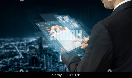 A business professional interacts with a transparent tablet displaying data analytics. The futuristic scene combines technology and urban nightlife Stock Photo