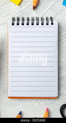 Blank notepad on a table with colored pencils and sticky notes nearby Stock Photo