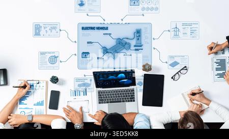 A dynamic workspace showcasing a team discussing electric vehicle innovation with laptops and notebooks. The environment promotes creativity and Stock Photo