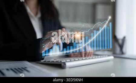A focused business professional examines financial trends with interactive digital graphs in a modern office, illustrating data analysis and growth Stock Photo