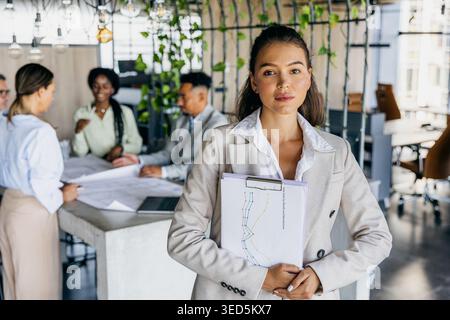 Confident Female Authority Figure Leads And Organizes Team Efforts During Meeting With Documents And Direction Stock Photo
