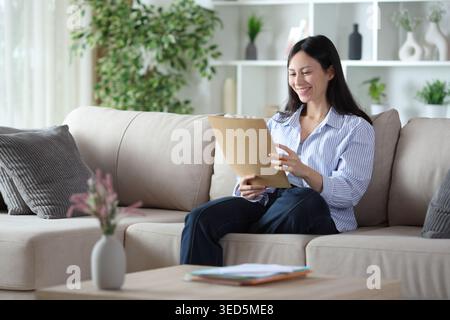 Asian woman checking paper document sitting on a sofa at home Stock Photo