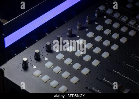 Close up view of a modern mixing console featuring an illuminated blue display with hui mode selected text and several control knobs. Professional aud Stock Photo