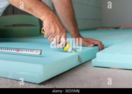 Worker on a construction site, cutting insulation boards before laying and fixing on a concrete floor Stock Photo