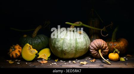 Mixed pumpkins with sliced pieces arranged on rustic table near blue wall. Autumn composition with squash vegetables and textured wooden background Stock Photo
