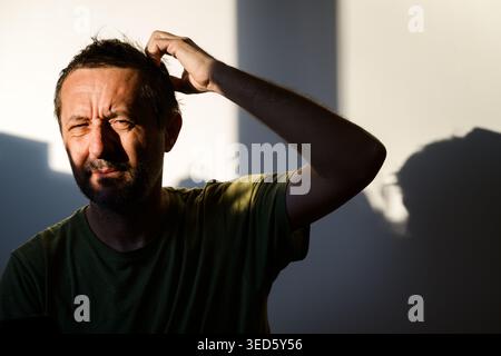 Portrait of a middle-aged man with short dark hair and beard, one hand scratching the top of his head in a gesture of confusion, frustration or deep t Stock Photo