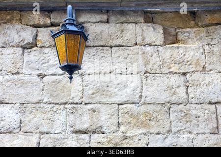 Vintage Lantern on Stone Wall. Old-fashioned hanging lantern with amber glass mounted against a weathered stone wall, creating a rustic architectural Stock Photo