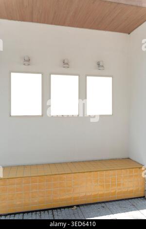 Three blank poster frames mounted on a textured wall with individual lights above and a yellow tiled bench below, ideal for advertising, menu design, Stock Photo
