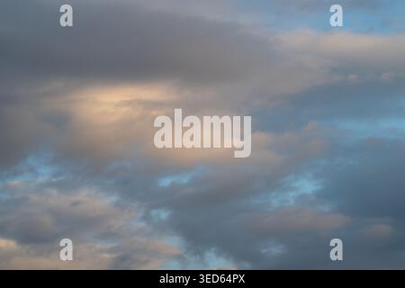 Soft sunrise clouds fill morning sky, muted golden light breaking through layered gray clouds, textured formations creating tranquil cinematic atmosph Stock Photo