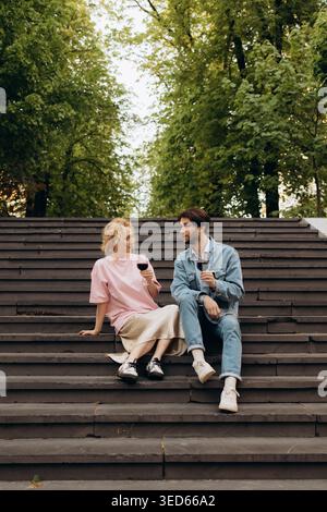 Young Couple Drinking Red Wine Sitting on Steps in Park Stock Photo