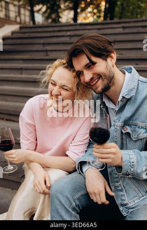 Happy young couple drinking red wine outdoors, laughing Stock Photo