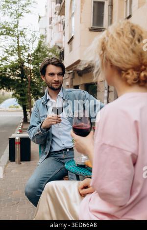 Young Man Holding Glass of Red Wine While Talking to Woman Stock Photo