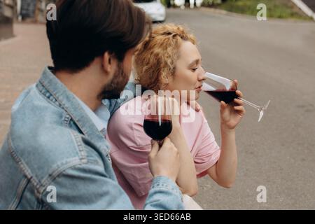 Woman Drinking Red Wine While Sitting with Man on City Street Stock Photo
