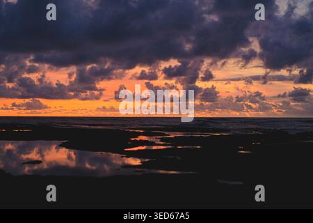 Orange and purple sunset over rocky coastline with reflections, Bali Stock Photo