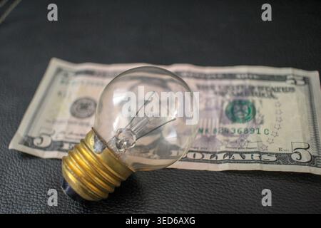 Financial concept showing a light bulb and money, representing the need for energy efficiency and smart household budgeting to fight high utility cost Stock Photo