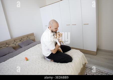 Man sitting on a sofa and caresses ginger tabby cat. Male person and cat pet resting together Stock Photo