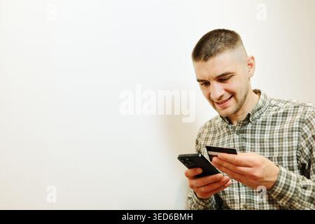 Man holds a bank card and smartphone while making an online payment at home. Concept of digital banking, mobile shopping and secure online Stock Photo