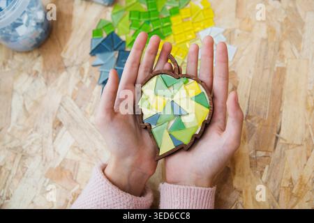 kid hands hold crafts mosaic against a gray background. mosaic master. childrens creative Stock Photo