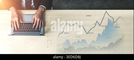 A businessman works on a laptop, analyzing financial data displayed as graphs on a wooden desk. The image captures the essence of modern business Stock Photo