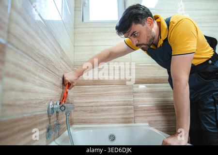 Plumber working on pipes and using a pipe wrench in a bathroom Stock Photo