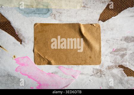 Blank Brown Kraft Paper Label over a Dirty Board with Ripped White and Pink Paper Fragments Stock Photo