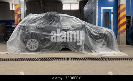 Vehicle fully wrapped in protective plastic film in a repair shop, prepared for painting or detailing process. Stock Photo