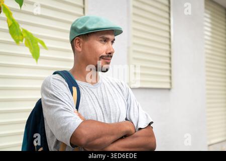 Smiling man wearing a flat cap and backpack, standing relaxed with arms crossed,  copy space Stock Photo