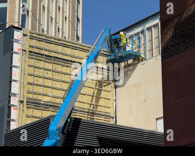 Leicester, UK - March 13, 2026: Construction worker on cherry picker repairing insulated building facade, Leicester Stock Photo