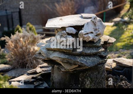 Stack of flat stones arranged as small garden structure on wooden stump outdoors in sunlight. Landscaping and natural decoration. Stock Photo
