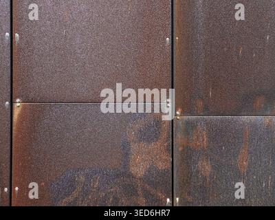 Wall of weathered Corten steel panels arranged in a grid, secured with small bolts, showing a uniform rusty texture. Stock Photo
