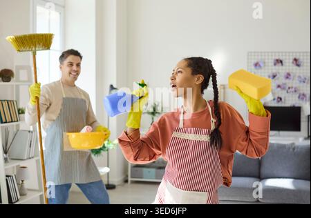 Happy couple cleaning at home, singing and dancing during fun housekeeping chores Stock Photo