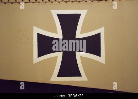 Black iron cross symbol with white outline painted on a beige surface in vintage military style. Close-up geometric cross design with strong contrast. Stock Photo
