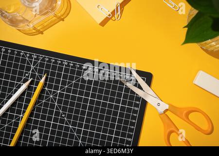 Top view of stationery supplies on a bright yellow background. Cutting mat, scissors, pencils, and clips. Copyspace Stock Photo