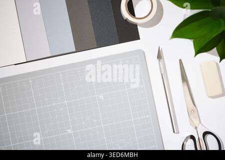 Craft workspace with cutting mat, utility knife, scissors, color samples and stationery on clean white background. Copyspace Stock Photo