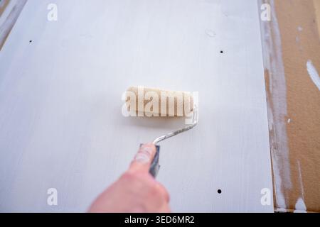 Hand painting drywall with roller applying white primer over patched surface, visible screw indentations Stock Photo