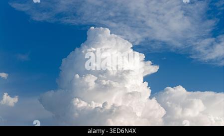 A single large, puffy, white cumulus cloud illuminated by the bright sunlight in the blue sky. Stock Photo