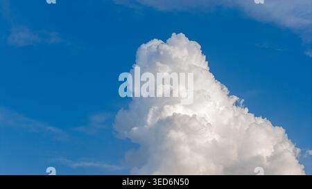 A single large, puffy, white cumulus cloud illuminated by sunlight in the blue sky. A textured and voluminous image. Stock Photo