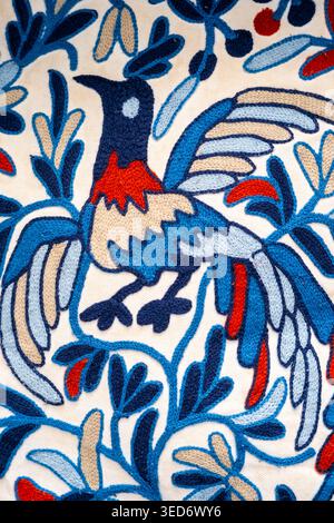 Artistic textile pattern featuring decorative bird illustration combined with floral ornamental motifs in blue, red, and white tones. Stock Photo