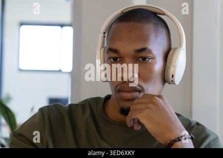 African American man wearing white headset and olive shirt resting chin showing bracelet at window Stock Photo