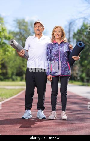 Mature man and woman with exercise mats posing in a park Stock Photo